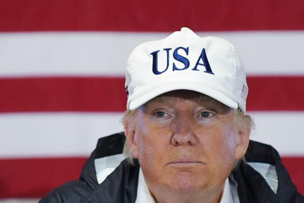 US President Donald Trump in front of the American flag wearing a white cap saying "USA."