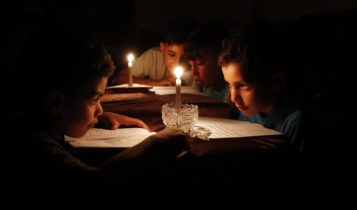 Palestinian children at home reading books by candle light due to electricity shortages in Gaza City.