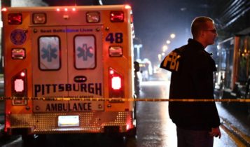 An FBI agent stands behind a police cordon and an ambulance outside the Tree of Life Synagogue (L) after a shooting there left 11 people dead in the Squirrel Hill neighborhood of Pittsburgh on October 27, 2018