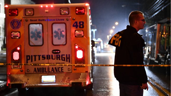 An FBI agent stands behind a police cordon and an ambulance outside the Tree of Life Synagogue (L) after a shooting there left 11 people dead in the Squirrel Hill neighborhood of Pittsburgh on October 27, 2018