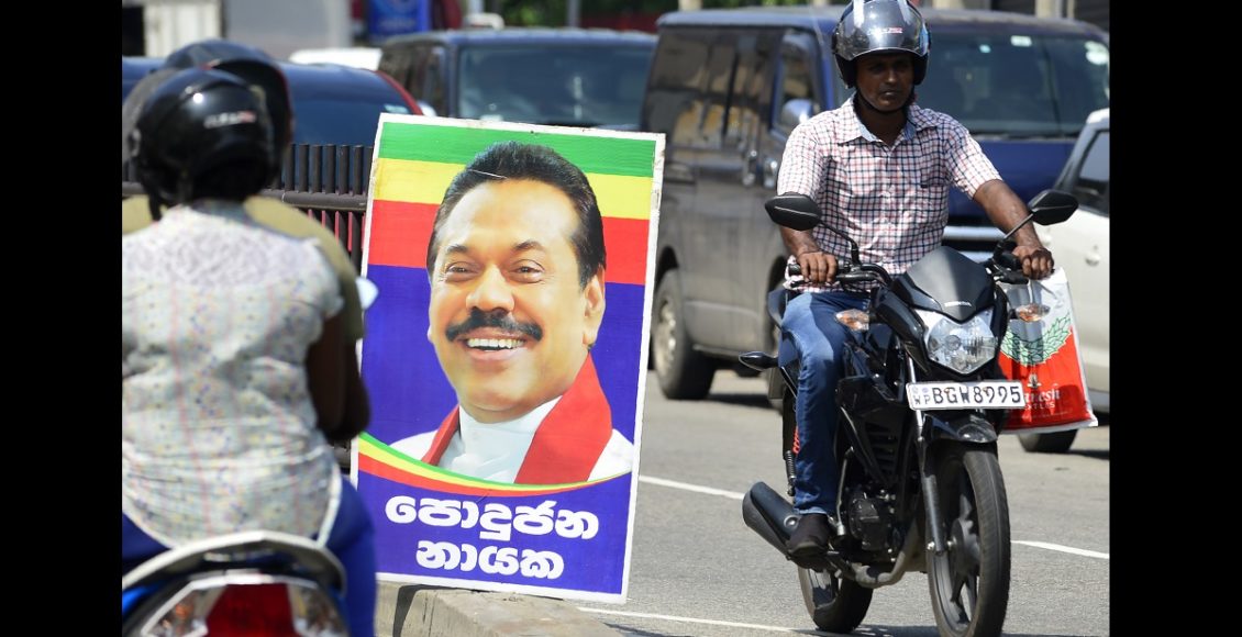 Sri Lankan motorcyclists ride past a poster of Mahinda Rajapakse's after he was sworn in as prime minister in Colombo on October 27, 2018