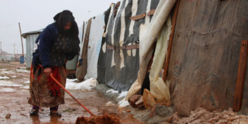 A Syrian refugee shovels mud in front of a makeshift shelter in an unofficial camp for Syrian refugees in Lebanon's Bekaa Valley