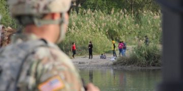 A soldier looks across the Rio Grande River from Texas into Mexico, where a group of people hang out on the river bank. Photo: Thomas Watkins, AFPA soldier looks across the Rio Grande River from Texas into Mexico, where a group of people hang out on the river bank