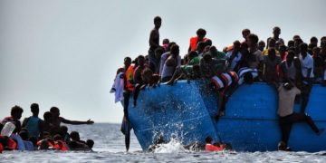 Migrants hang from a boat as they wait to be rescued in the Mediterranean Sea, some 12 nautical miles north of Libya,