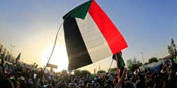 Protestors in Sudan wave a giant Sudanese flag above a crows of demonstrators