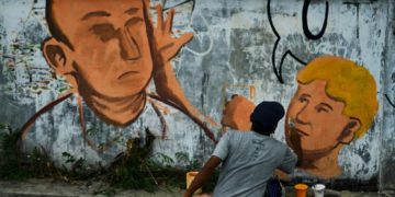 An artist paints a mural in Indonesia depicting Australian Sen. Fraser Anning being hit in the head with an egg by William Conolly.