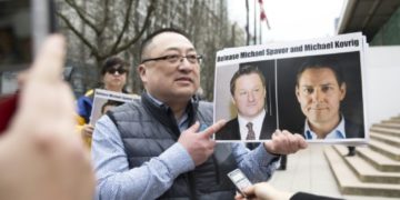 An activist holds photos of Michael Kovrig and Michael Spavor who are being held by China.