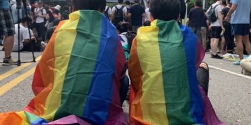 Two LGTB rights supporters covered in rainbow flags attend Taipei's same-sex marriage gathering