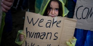 Refugee child holding up a sign reading 'we are human like you'