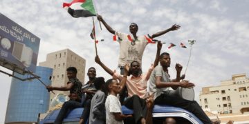 Protestors in Sudan wave a flag while sitting on top of a car