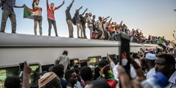 Sudanese protesters from the city of Atbara, flash the V-sign for victory and wave national flags atop a train, as it arrives at the Bahari station in Khartoum