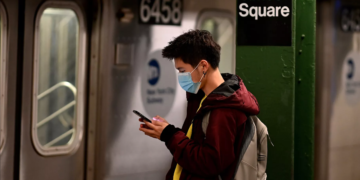A man wearing a face mask looks at his phone in the New York metro during the coronavirus outbreak.