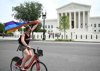 A man waves a rainbow flag as he rides by the US Supreme Court that released a decision that says federal law protects LGBTQ workers from discrimination on June 15, 2020 in Washington,DC.