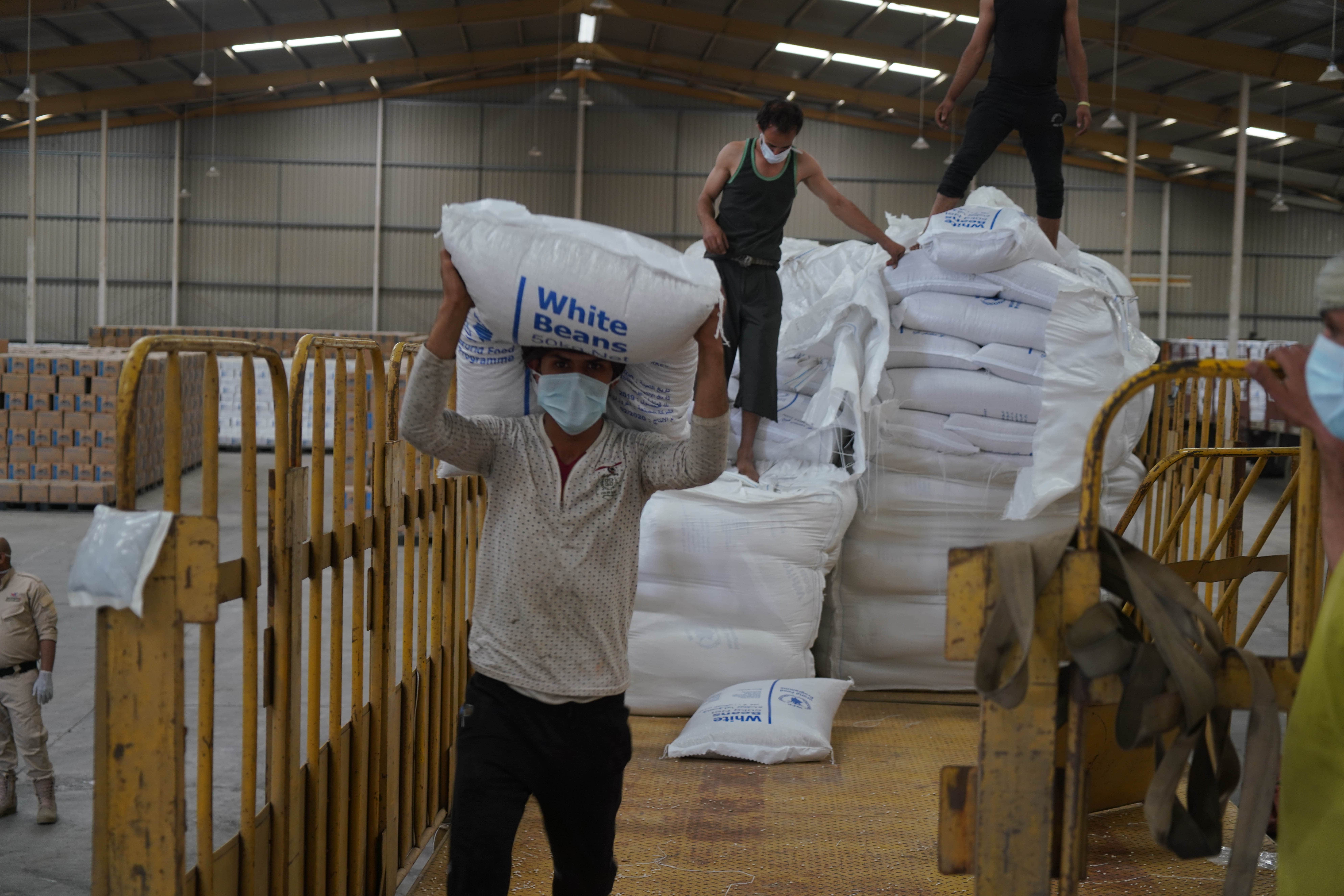 A man carries a bag of white beans in a WFP warehouse in Sana'a, Yemen