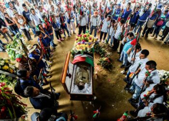 A ring of people mourn around an open casket