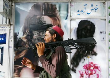 A Taliban fighter walks past a beauty saloon with images of women defaced using a spray paint in Shar-e-Naw in Kabul on August 18, 2021