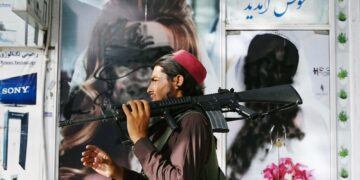 A Taliban fighter walks past a beauty saloon with images of women defaced using a spray paint in Shar-e-Naw in Kabul on August 18, 2021