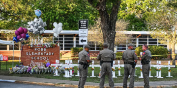 Officers in Uvalde, Texas, stand outside Robb Elementary School near a makeshift memorial for the shooting victims