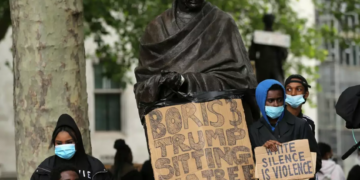 Protesters stand with placards in front of the statue of India's independence leader Mahatma Gandhi in Parliament Square, central London, after a demonstration outside the US Embassy