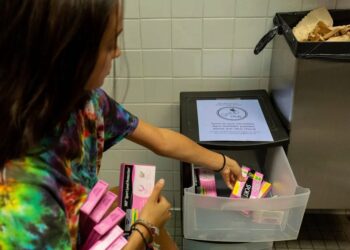 A woman stocks a bathroom with free pads and tampons