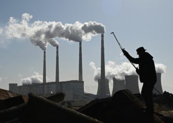 A worker cutting steel pipes near a coal-powered power station