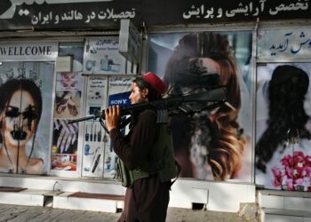 A Taliban fighter walks past a beauty parlor